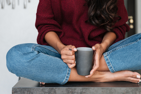 Close up of a woman sitting on a kitchen table and holding cup of coffeeの写真素材