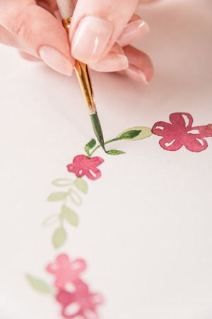 Close up of young artist drawing flowers pattern with watercolor paint and brush on paper at workplaceの写真素材