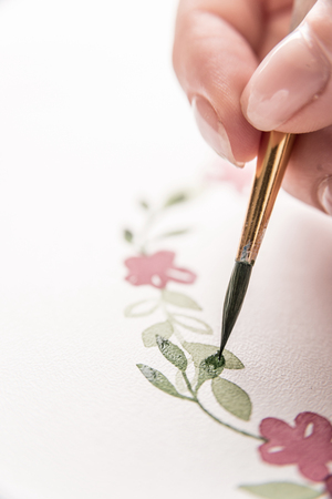 Close up of young artist drawing flowers pattern with watercolor paint and brush on paper at workplaceの写真素材
