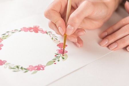 Close up of young artist drawing flowers pattern with watercolor paint and brush on paper at workplaceの写真素材