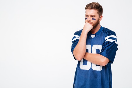 Thoughtful serious male fan in blue t-shirt standing isolated over white background. Looking aside.の写真素材