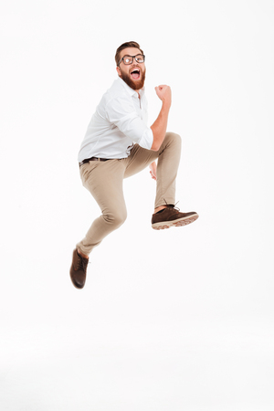 Photo of cheerful young bearded man jumping over white wall background isolated. Looking camera.の写真素材