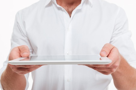 Cropped image of young man standing over white wall background isolated. Give you a tablet computer.