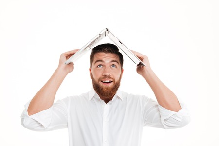 Picture of handsome young bearded man standing over white wall background isolated. Looking aside holding laptop.の写真素材