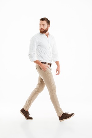Picture of handsome young bearded man walking over white wall background isolated. Looking aside.の写真素材