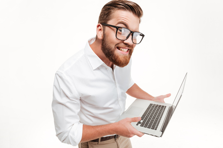 Funny bearded man in eyeglasses holding laptop and staring at camera isolated over white backgroundの写真素材