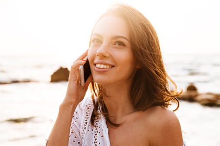 Close up image of woman in lught summer dress talking on smartphone while being on beachの写真素材