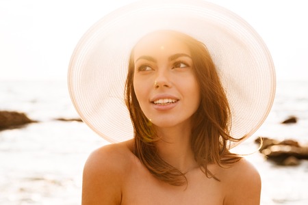 Close up portrait of beautiful woman in hat posing near the sea and looking awayの写真素材