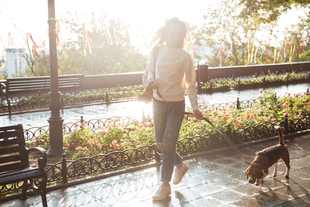 Full length image of happy brunette woman in autumn clothes and eyeglasses walking with her dog in parkの写真素材