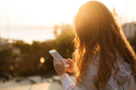 Side view of brunette woman in autumn clothes writing message on her smartphone outdoorsの写真素材