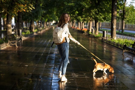 Full length back view image of happy brunette woman in autumn clothes walks with dog in park and looking at the cameraの写真素材