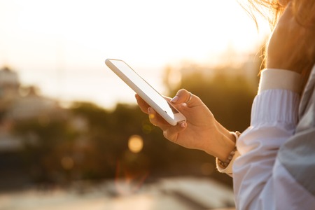 Cropped image of woman in autumn clothes usin her smartphone outdoors. Side viewの写真素材