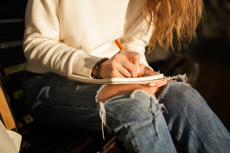 Cropped image of woman in autumn clothes sitting on bench and writing somethingの写真素材