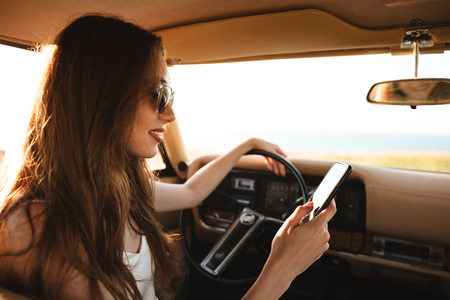 Photo from car of smiling brunette woman in singlasses using smartphoneの写真素材