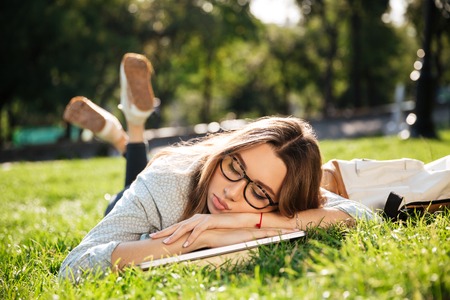 Young brunette in eyeglasses sleeping on grass in park with laptop computerの写真素材