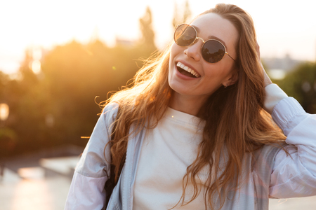 Close up picture of laughing brunette woman in sunglasses and autumn clothes posing outdoors and looking at the cameraの写真素材