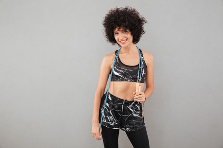 Smiling fitness woman posing with jumping rope and looking at the camera over gray backgroundの写真素材