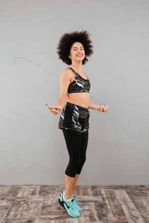 Full length picture of young fitness woman doing exercise with jumping rope