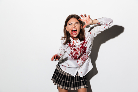 Scary zombie girl covered with blood stains ready to attack with a large knife isolated over white backgroundの写真素材