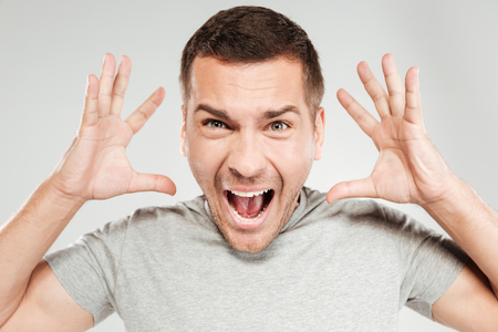 Photo of young screaming man dressed in grey t-shirt isolated over grey wall. Looking camera.の写真素材
