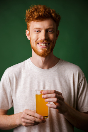 Portrait of handsome bearded man holding glass of orange juice , over green backgroundの写真素材