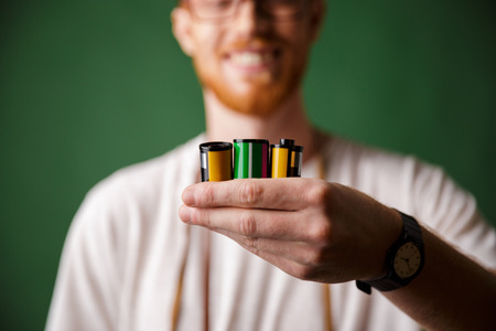 Cropped photo of readhead bearded photographer, holding camera rolls, selective focus