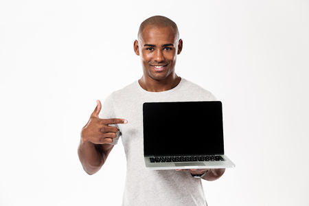 Photo of cheerful young african man standing isolated over white background showing display of laptop computer. Looking camera.の写真素材
