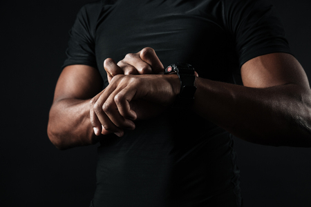 Close-up photo of african man in black t-shirt check out time at black wristwatch, over black backgroundの写真素材