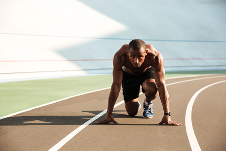 Portrait of a fit athletic afro american sportsman about to start his run on a track field outdoorsの写真素材
