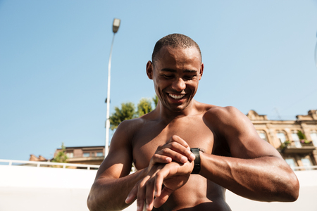 Half naked afro american musculary sports man checking time on wristwatch after workoutの写真素材