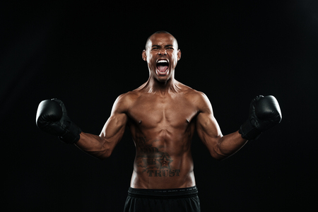 Afro american boxer celebrating his victory with raised arms in black gloves, isolated on black backgroundの写真素材