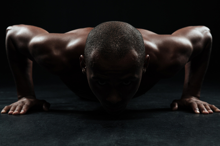 Close-up portrait of afro american sports man, doing pushup exercise in black interiorの写真素材