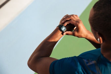 Top view close up of a fit african sportsman looking at his wrist watch while standing on a track...