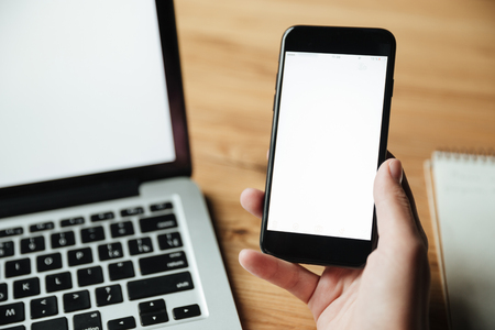 Cropped image of woman sitting by the table with laptop computer and holding smartphoneの写真素材