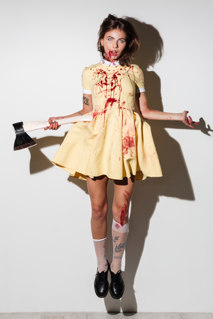 Full length image of young frightening zombie woman in dress like flying with an axe in hand and looking at the camera over white backgroundの写真素材