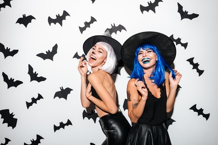 Image of two emotional young women in halloween costumes on party over white background. Looking aside.の写真素材