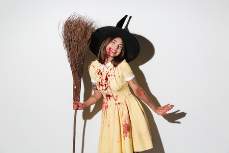 Smiling woman in halloween costume like witch holding broom and looking at the camera over white backgroundの写真素材