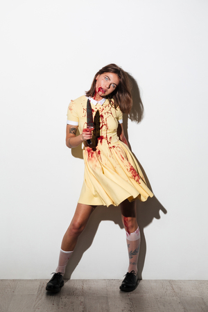 Full length image of crazy zombie woman in dress with knife looking at the camera over white backgroundの写真素材
