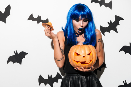 Picture of emotional gorgeous young woman in witch halloween costume on party over white background with pumpkin. Looking aside.の写真素材