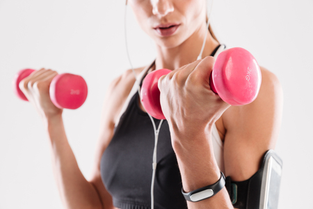Close up portrait of a young fitness woman doing exercises with dumbbells isolated over white backgroundの写真素材