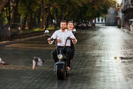 Full length image of happy business couple rides on modern motorbike in park