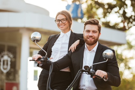 Happy business couple posing with modern motorbike outdoors and looking at the cameraの写真素材