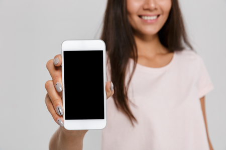 Close up portrait of a smiling pretty asian woman showing blank screen mobile phone isolated over white backgroundの写真素材