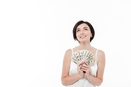 Portrait of a happy smiling woman holding bunch of money banknotes and looking up isolated over...