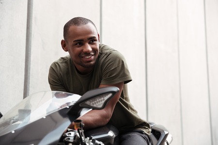 Portrait of a smiling young afro american man sitting on a motorcycle and looking away outdoors