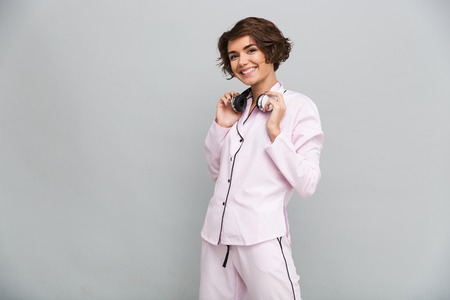 Portrait of a cheerful smiling girl in pajamas with headphones standing and looking at camera...
