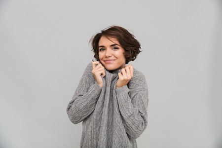 Picture of cheerful young lady dressed in sweater standing isolated over grey background. Looking camera.の写真素材
