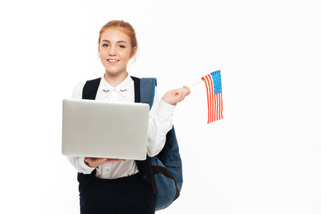 Smiling gigner student woman with backpack holding laptop computer and USA flag while looking at the camera over white backgroundの写真素材