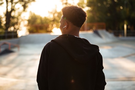 Back view of a young african man in earphones outdoors