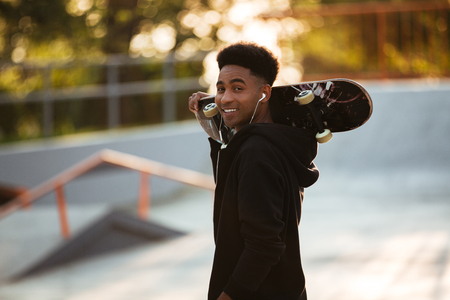 Smiling young male teenager guy holding skateboard on shoulders and looking at camera outdoorsの写真素材